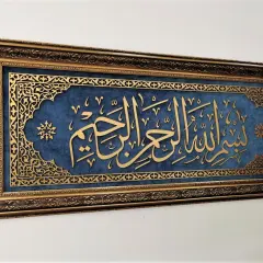 Złota kaligrafia "Bismillah" na granatowym tle, w bogatej, zdobionej ramie.