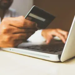 Mężczyzna z kartą kredytową w dłoni wpisuje dane na laptopie, realizując swój hedonizm w zakupach online.