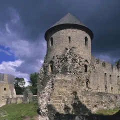 Ruiny zamku w **Inflantach** pod burzliwym niebem. Kamienne mury i wieże, częściowo zniszczone, świadczą o dawnej potędze.