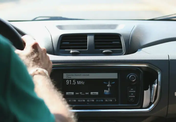 Ręce na kierownicy, radio samochodowe pokazuje 91.5 MHz. Wygodne środki masowego przekazu w podróży.