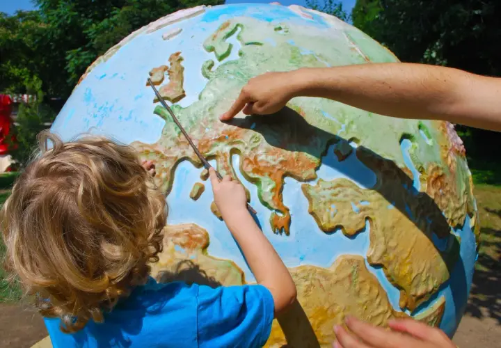 Dziecko i dorosły wskazują na mapę Europy na globusie, ucząc się geografii.