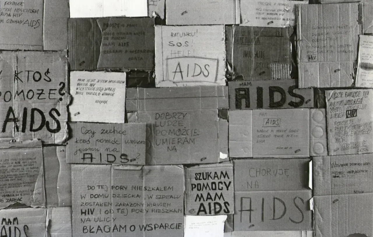 Ludzie błagają o pomoc, umierają na AIDS. Kartony z napisami "SOS", "Help", "Proszę o pomoc" świadczą o desperacji i walce o życie w obliczu choroby, która w tamtych czasach była naznaczona stygmatyzacją i brakiem wsparcia, tworząc swoistą **hegemonię*...
