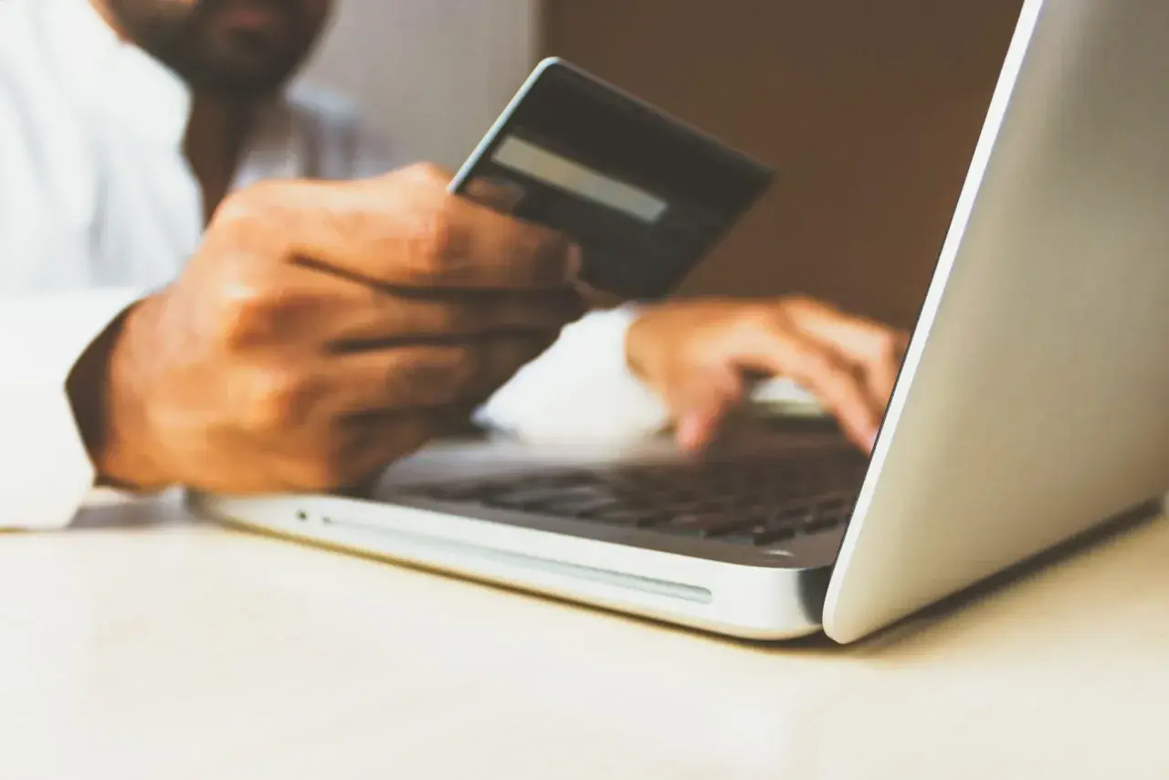 Mężczyzna z kartą kredytową w dłoni wpisuje dane na laptopie, realizując swój hedonizm w zakupach online.